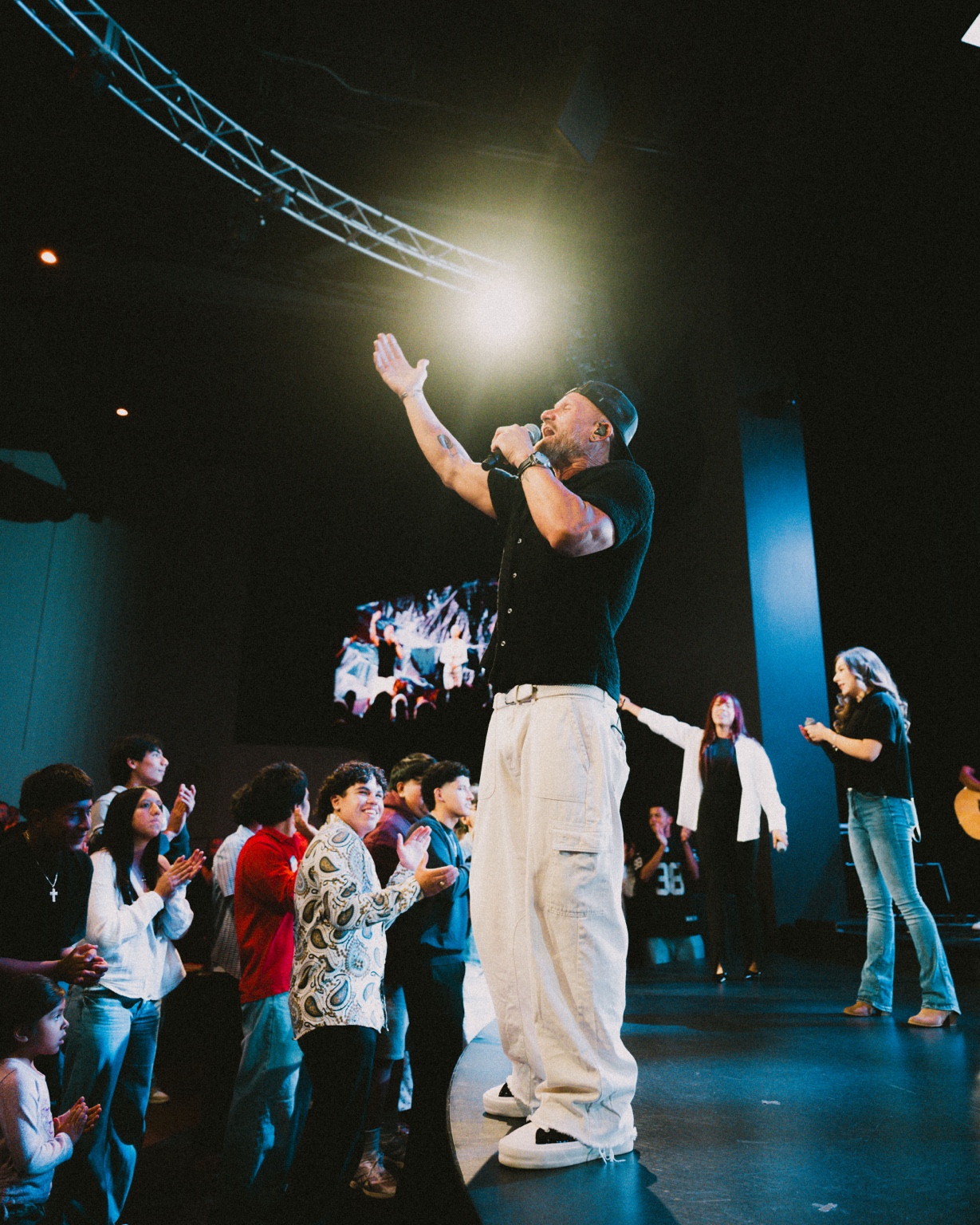 Justin leading worship with one hand raised as people worship around him