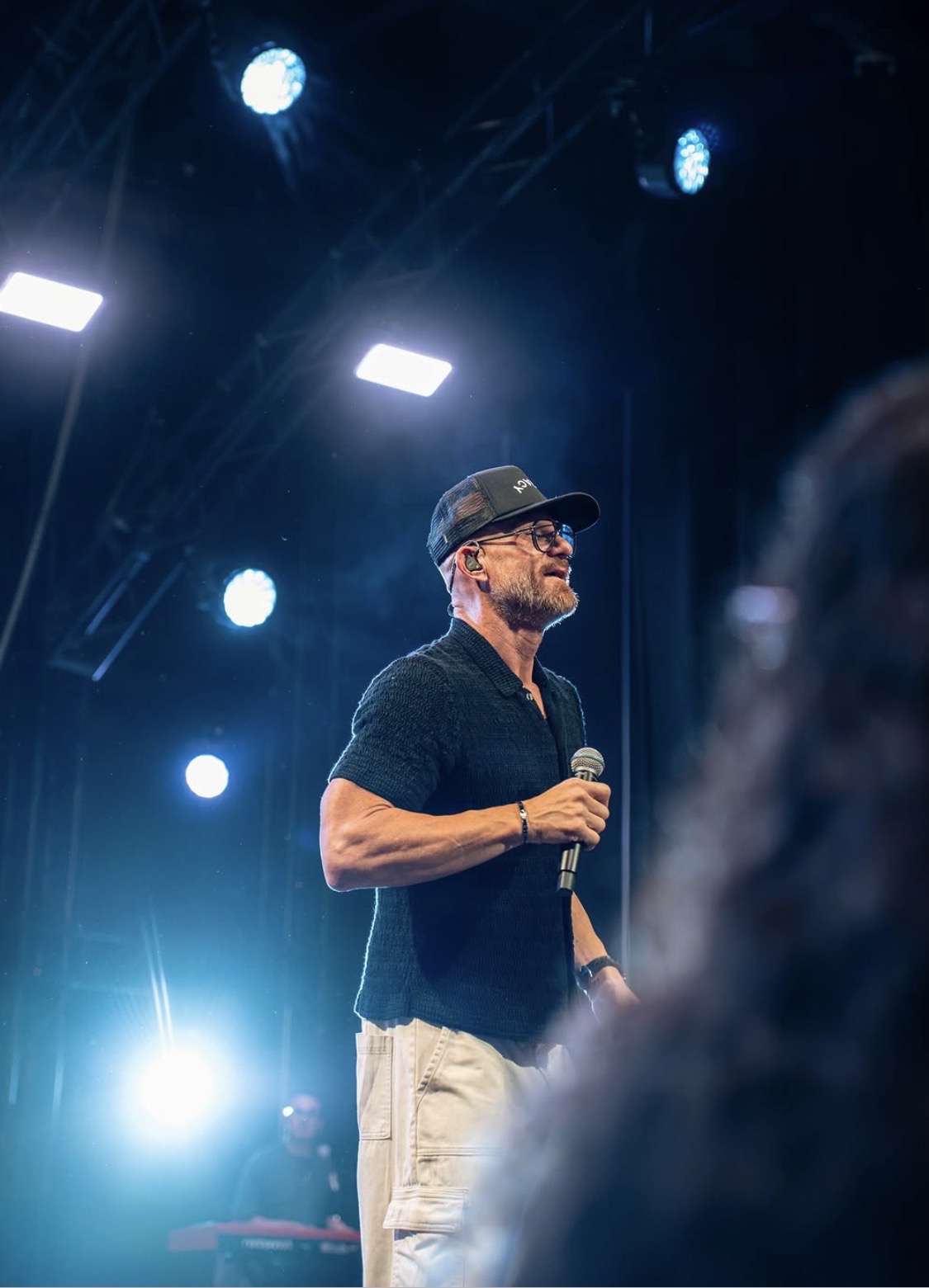 Justin Howard onstage with a microphone beneath blue lights